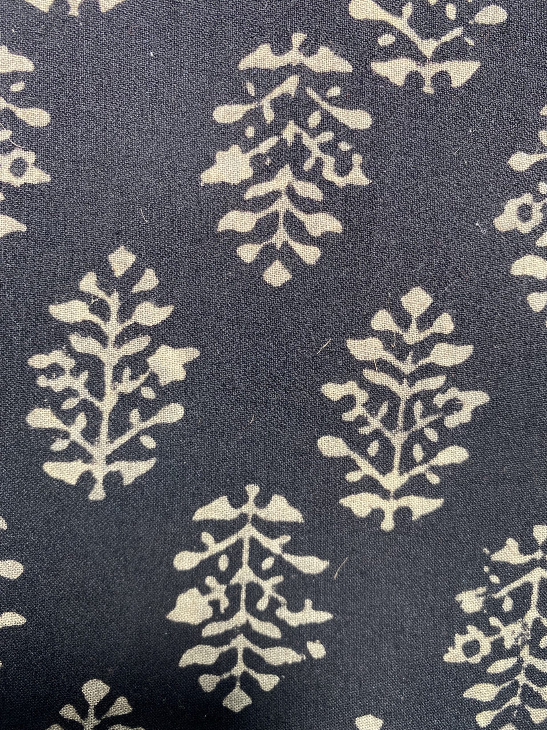 Close-up of navy fabric with a repeating cream botanical pattern resembling stylized flowers or snowflakes on blue background.