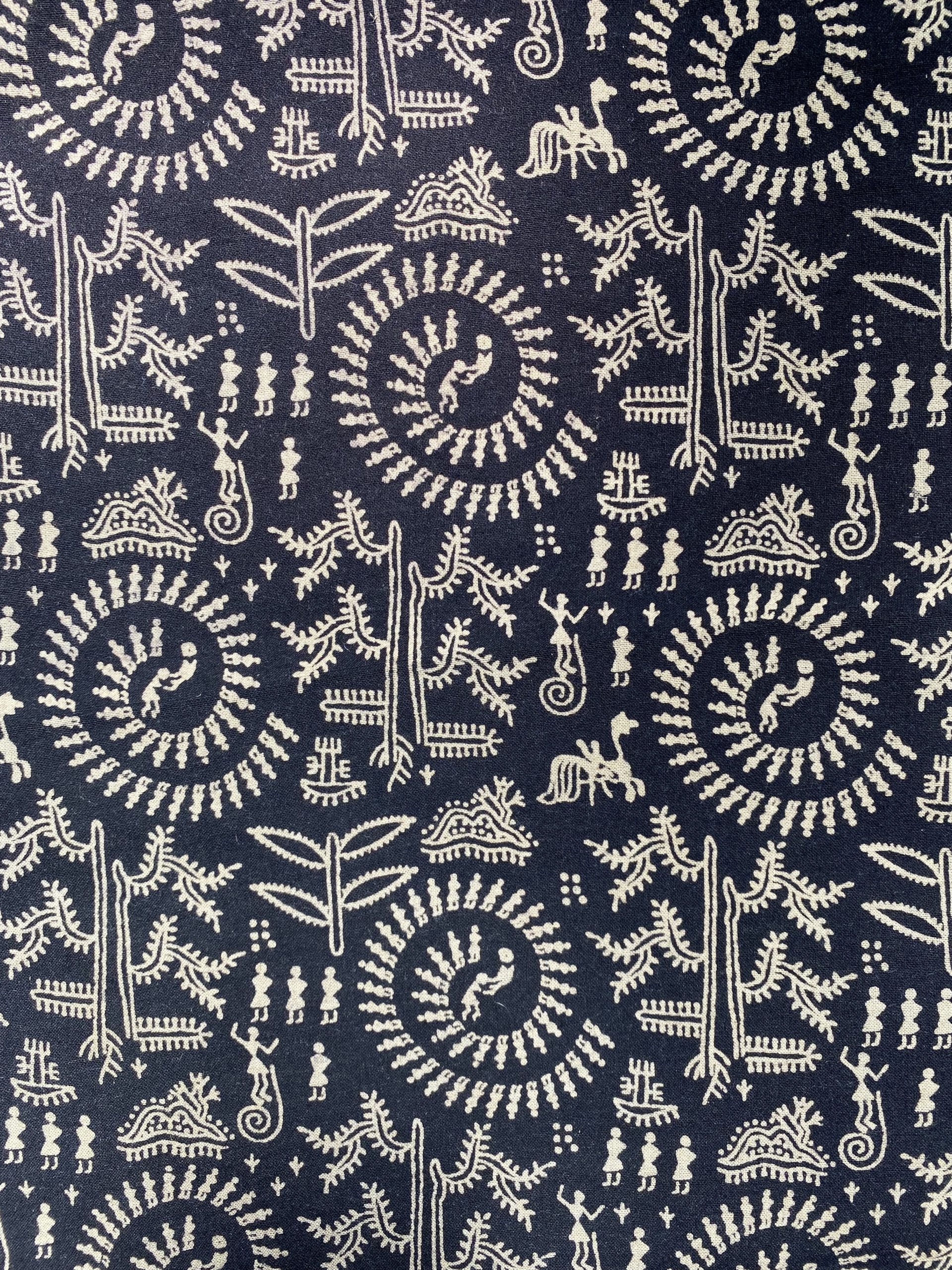 Decorative black fabric with white folk-art motifs including spirals, trees, and tiny people depicted in traditional warli art from India