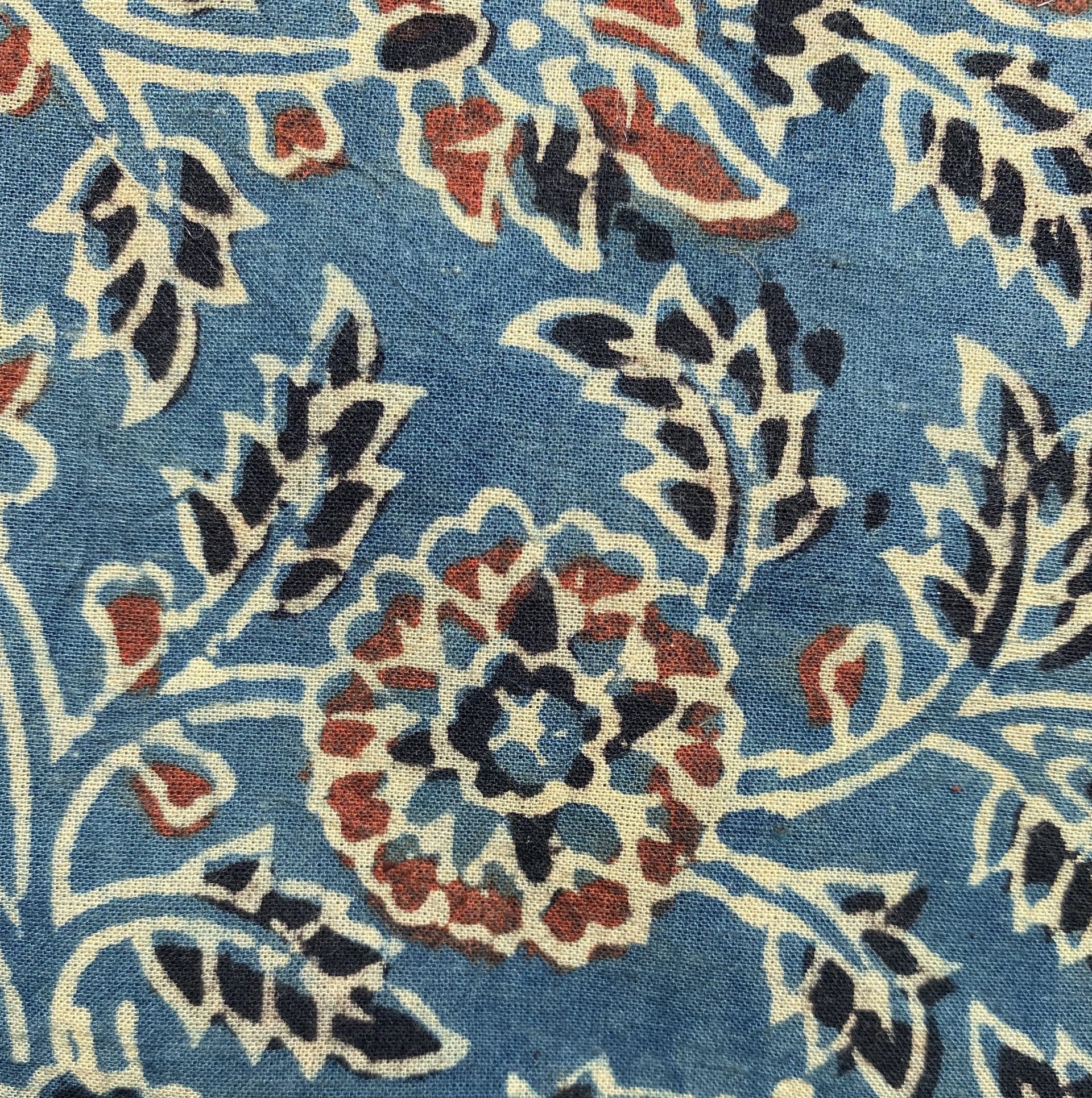 Close-up of blue fabric with cream floral scrolls and red and black accents.