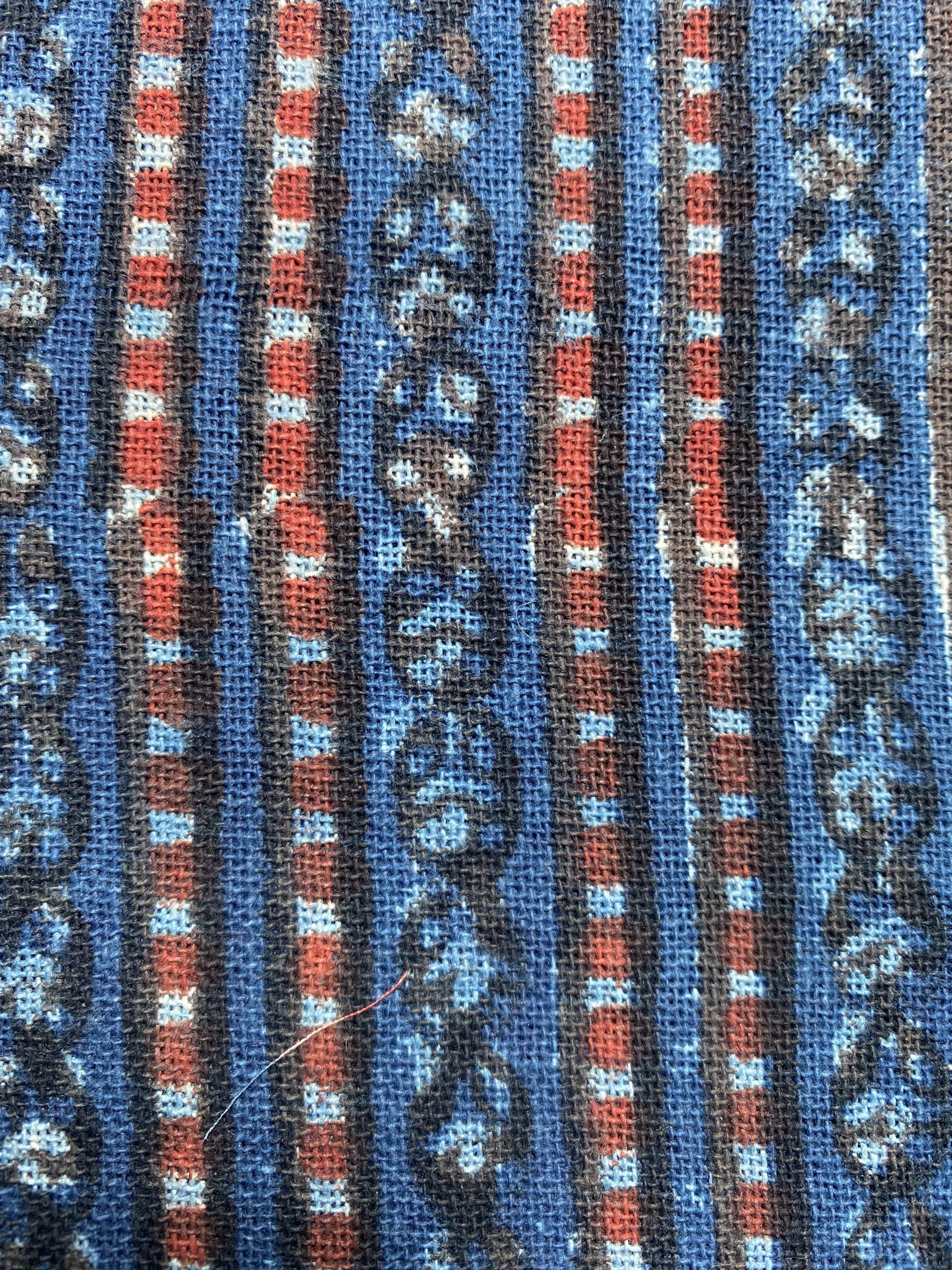 Close-up of a woven textile with blue fields and red-brown geometric stripes.