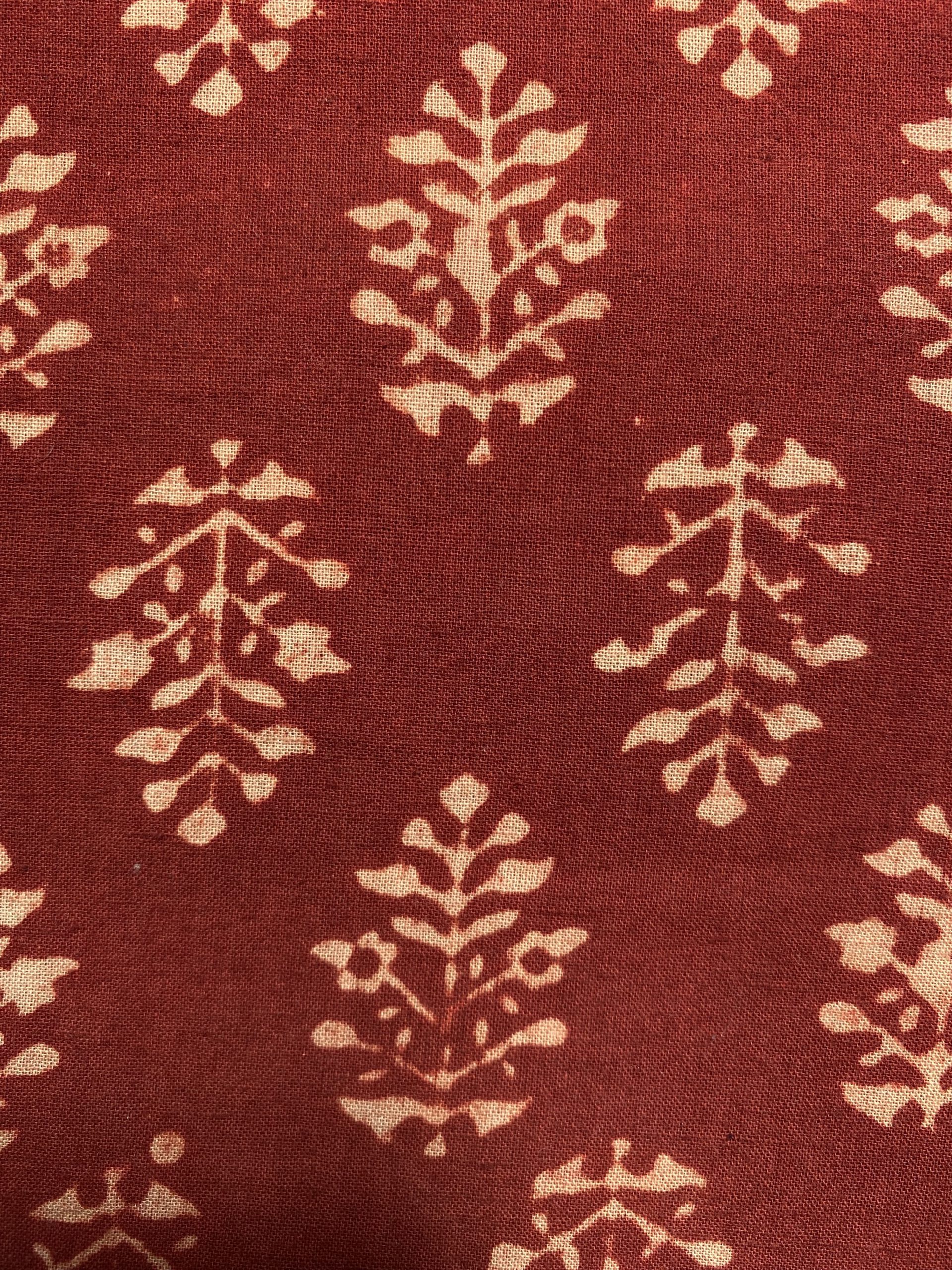 Red fabric with a cream floral damask-like pattern repeating across the surface, resembling decorative upholstery fabric.