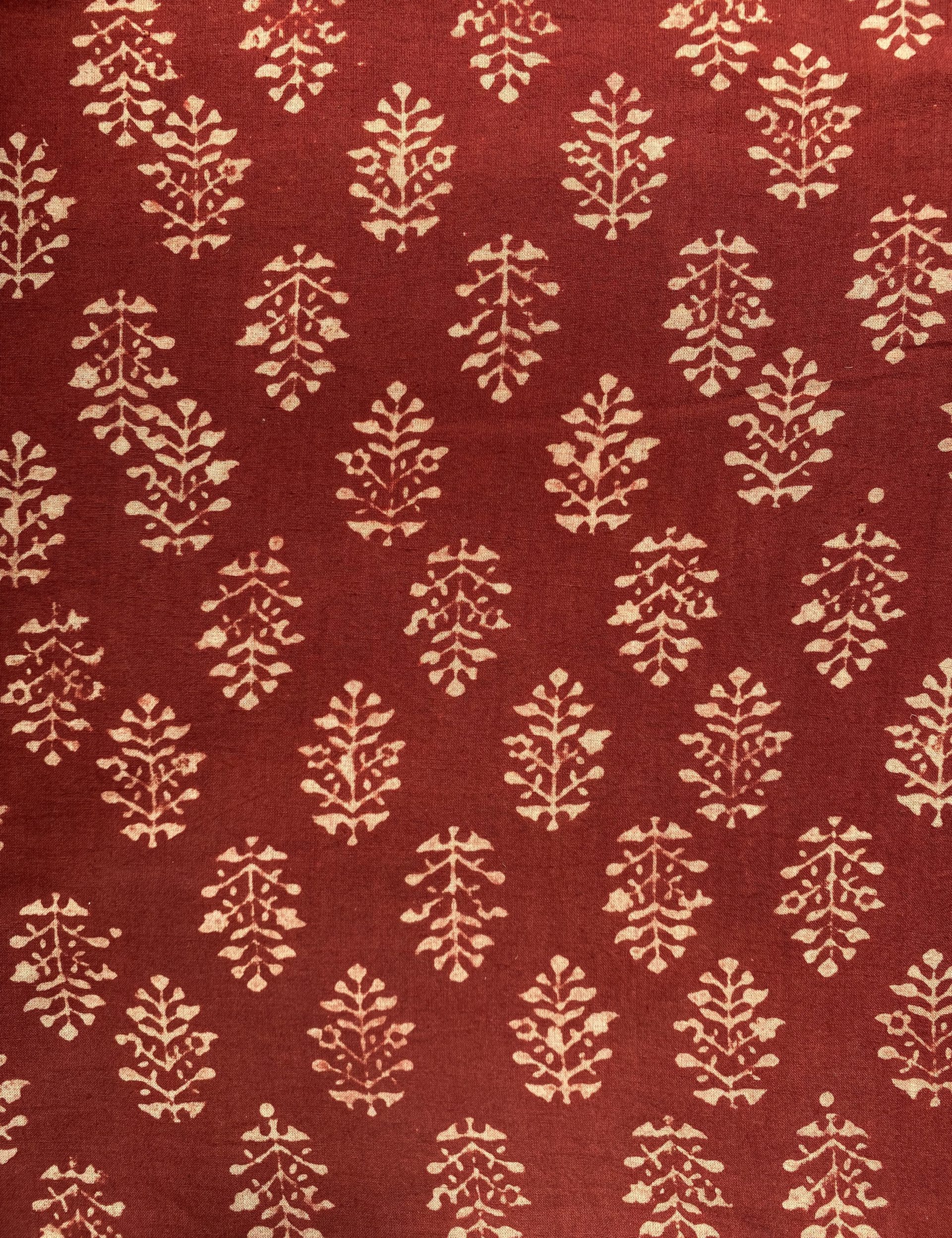 Red textile with repeating cream botanical motifs of symmetrical leafy sprigs on maroon background.