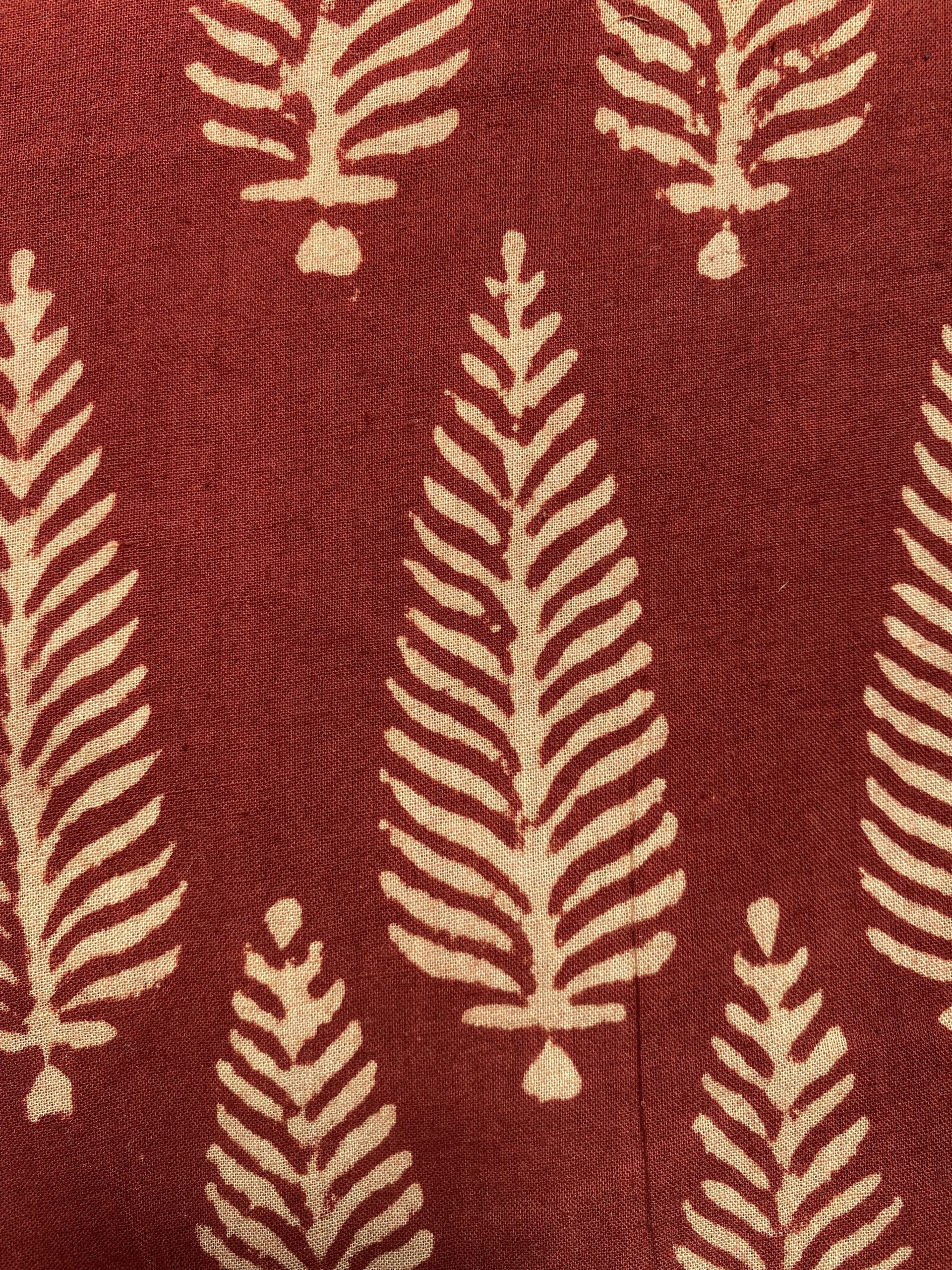 Close-up of red fabric with a beige fern-like leaf pattern repeating vertically.