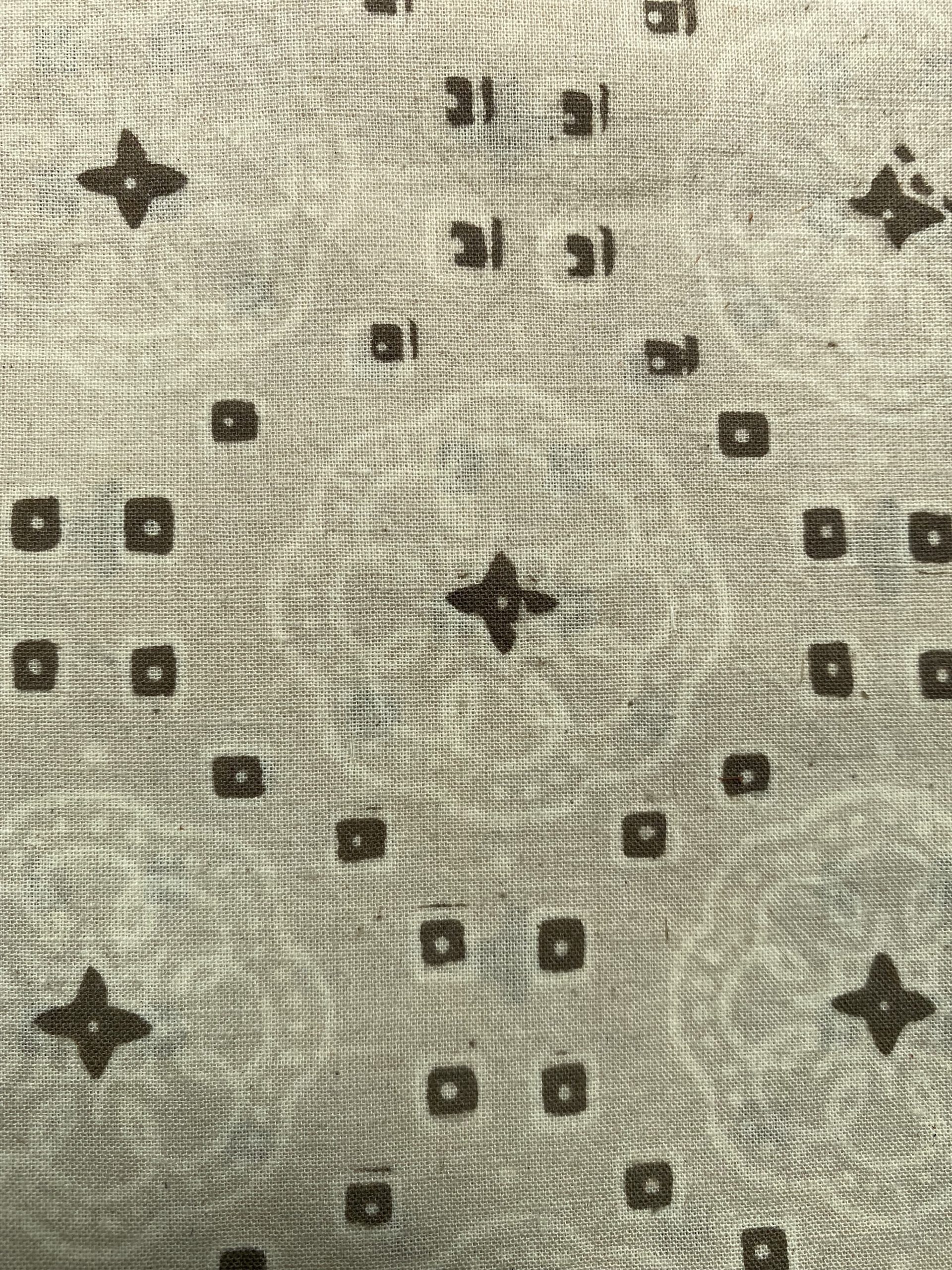 Close-up of beige woven fabric with a repeating dark square and four-point star pattern similar to a designer print.