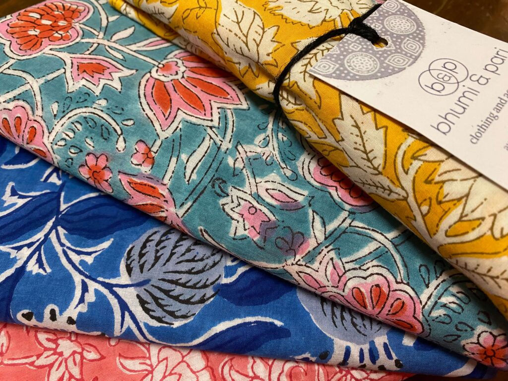 Close-up of folded floral fabric in blue, pink, and coral with a white tag attached.
