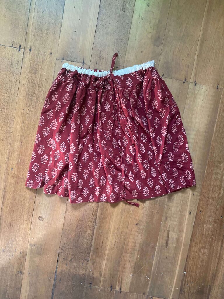 Maroon skirt with white leafy pattern and an elastic waist with tie, laid on a wooden floor.
