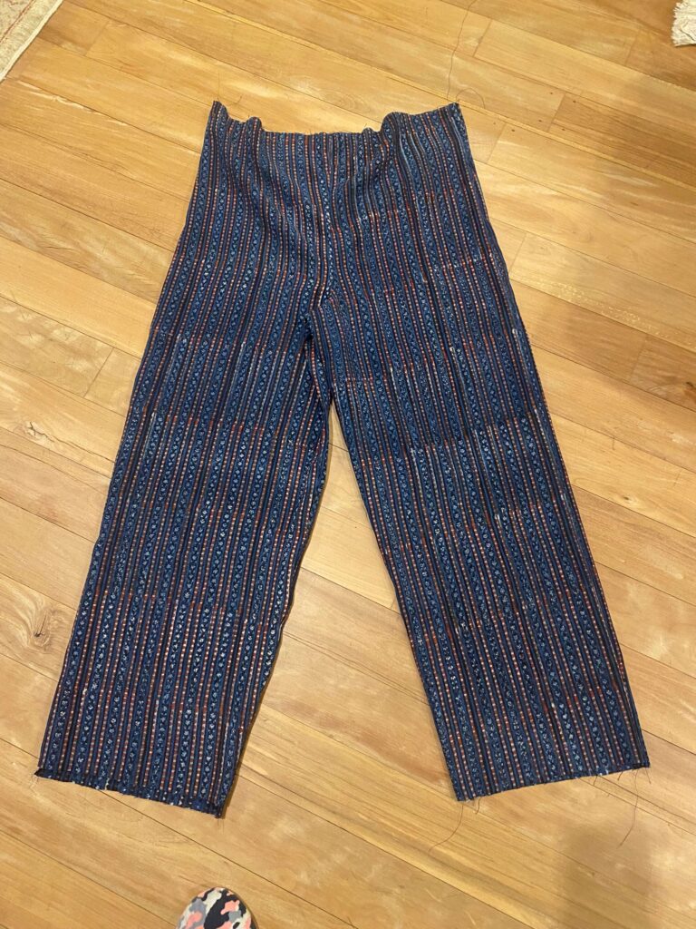 Blue patterned striped pants laid flat on a wooden floor, folded at the waist.