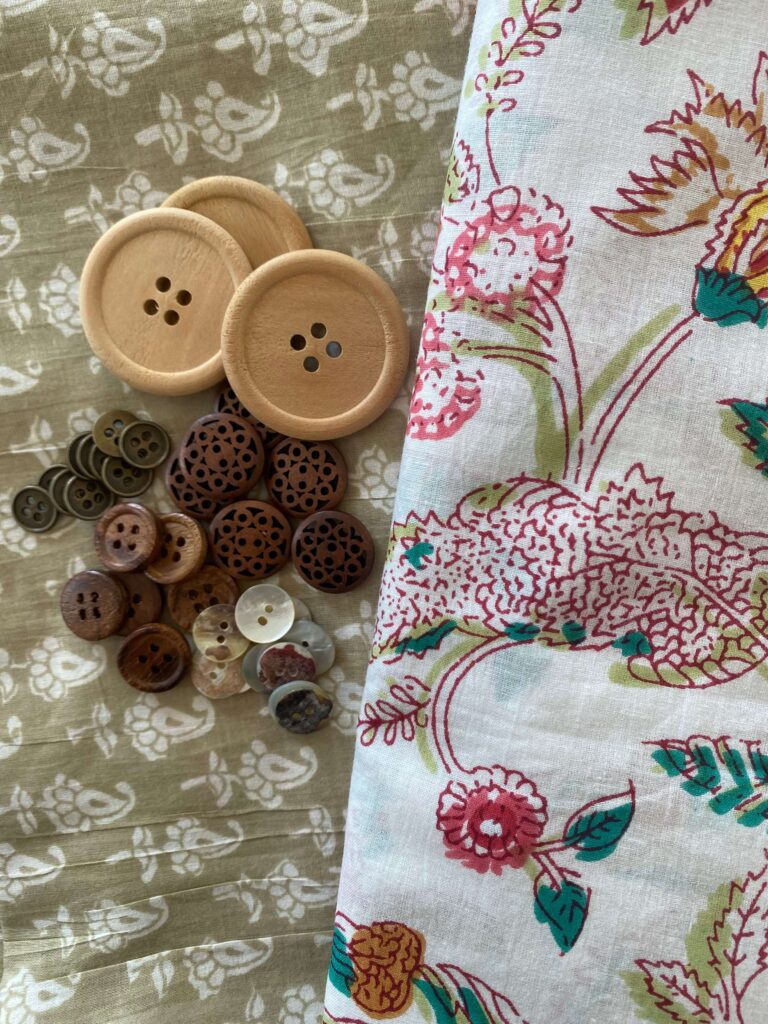 Two large round wooden buttons with four holes, surrounded by many smaller brown and ivory buttons on patterned fabrics